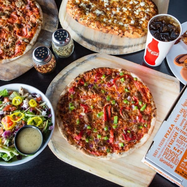 Three 1000 Degrees Pizza pies, a fresh salad, Coca-Cola, and spices on a dark table.