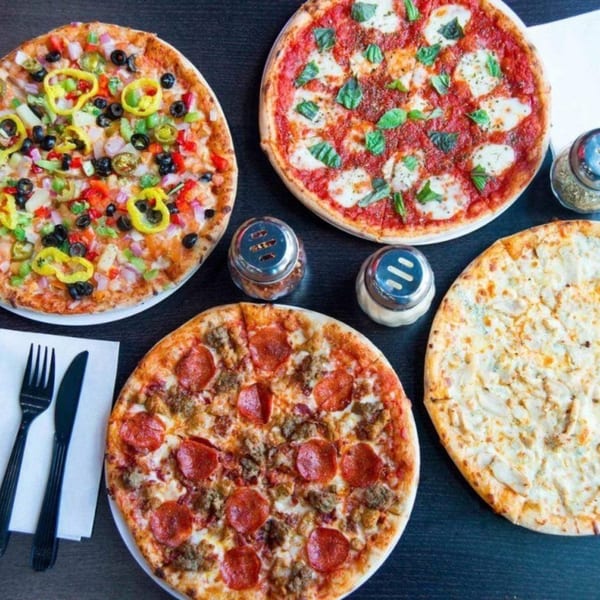 Four 1000 Degrees Pizza pies, including pepperoni, veggie, Margherita, and white chicken, on a dark table.