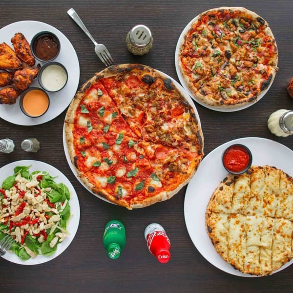 Two 1000 Degrees pizzas, wings, salad, and cheesy bread on a dark wooden table.